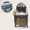 A baby is sleeping in a portable crib that can also be used as a playpen. The crib has a canopy with hanging toys and a side pocket for storage. A close-up inset shows a storage organizer attached to the side of the crib. Produktbild-Vorschau