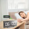 A woman is sleeping in bed next to a digital alarm clock on a nightstand. Produktbild-Vorschau