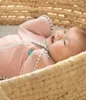 A baby lying in a woven basket, wearing a pink swaddle. Anteprima dell’immagine prodotto