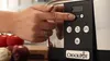 A hand is shown pressing buttons on a Crock-Pot slow cooker, with vegetables in the background. Produktbild-Vorschau