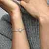A person's arm wearing a silver bracelet with a small charm. Podgląd zdjęcia produktu