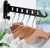 A black wall-mounted retractable clothes drying rack with several wooden hangers and white shirts hanging on it. Produktbild-Vorschau