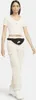 A woman wearing a cream crop top, cream cargo pants, and white sneakers, with a black Nike fanny pack around her waist. Náhled obrázku produktu