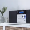 A Universum stereo system is displayed on a white cabinet with woven baskets. Produktbild-Vorschau