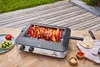 A rotisserie grill with meat cooking on it, placed on a wooden deck with some side dishes. Produktbild-Vorschau