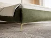 A close-up view of the corner of a green upholstered bed frame with gold legs, resting on a textured rug. Produktbild-Vorschau
