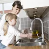 A woman and a child are in a kitchen, filling a glass with water from a faucet. Podgląd zdjęcia produktu