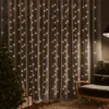 A room decorated for the holidays with a Christmas tree and presents, featuring a curtain of warm white LED lights. Produktbild-Vorschau