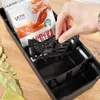 A hand is placing a black divider into a black organizer box containing spice packets. Bay leaves are scattered around the box. Anteprima dell’immagine prodotto