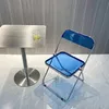 A blue folding chair and a small table with a drink on it, set against a textured wall. Produktbild-Vorschau