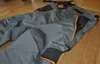 A pair of gray work pants with orange and black accents are laid out on a wooden floor. Produktbild-Vorschau