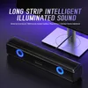A black soundbar with blue LED lights is placed in front of a computer monitor stand. Náhled obrázku produktu