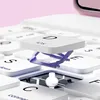 A close-up view of a white keyboard with a small, purple stand holding up a white square object with 'IOS' and 'D' printed on it. Náhľad obrázku produktu
