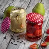 Two jars of preserved fruit, one with pears and the other with strawberries, are displayed on a wooden surface with whole pears and scattered cloves. Voir les images du produit