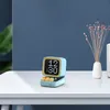 A small, retro-style digital clock with a screen displaying the time sits on a white table. Náhled obrázku produktu