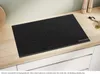 A black induction hob is shown on a wooden countertop, with kitchen utensils in the background. Anteprima dell’immagine prodotto