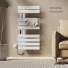 A white electric towel warmer is mounted on a light brown wall next to a beige sofa. A striped towel is draped over one of the bars of the warmer. A plant is visible on the left side of the image. Náhľad obrázku produktu