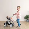 A young boy is pushing a twin doll stroller with two dolls inside. Produktbild-Vorschau