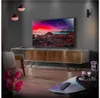 A modern living room with a large TV displaying a colorful landscape, a TV stand, a chair, and a coffee table with drinks. Produktbild-Vorschau