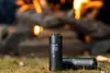 Two black portable air pumps are placed on the ground in front of a campfire. Podgląd zdjęcia produktu