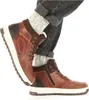 A close-up shot of a person wearing brown high-top boots and gray socks, with the legs of dark jeans visible. Anteprima dell’immagine prodotto