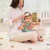 A woman is brushing a baby's hair while sitting on a rug. Produktbild-Vorschau