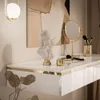 A close-up view of a white, high-gloss vanity table with gold trim, showcasing decorative items like a bust, a makeup mirror, and makeup brushes. Náhled obrázku produktu