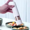 A hand is holding a white electric pepper grinder over a bowl of food. Podgląd zdjęcia produktu