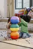 Two children are playing with a stack of colorful, rounded blocks on a rug in a room. Voir les images du produit