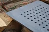 A close-up of a square metal grate with many small holes, resting on a pile of chopped wood. Anteprima dell’immagine prodotto