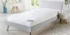 A white mattress topper is shown on a gray bed frame in a bedroom setting. Produktbild-Vorschau
