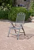 A metal folding chair sits on a brick patio in a garden setting. Produktbild-Vorschau