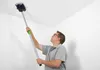 A man is using a Festool Tapetenperforierer TP 220 to prepare a ceiling for wallpapering. Podgląd zdjęcia produktu