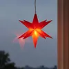 A red star-shaped lamp hangs in front of a window, casting a reflection. Produktbild-Vorschau