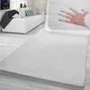 A white fluffy rug is shown in a living room setting with a white sofa and a hand pressing into the rug to show its softness.