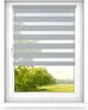 A window with a gray and white striped roller blind partially covering the view of a park with trees. Anteprima dell’immagine prodotto