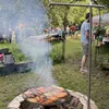An outdoor gathering with people, food being grilled, and tables set up. Podgląd zdjęcia produktu
