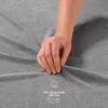 A hand is touching a grey fabric, likely a bedsheet, with text indicating the material composition. Produktbild-Vorschau