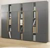 A large, modular gray cabinet with wood-tone accents, filled with books and binders, shown against a white wall and on a light wood floor. Produktbild-Vorschau