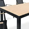 A close-up view of a wooden slatted table with a black metal frame, and parts of chairs visible. Produktbild-Vorschau