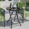 A round black glass-top folding table with two green chairs on a tiled patio. Produktbild-Vorschau