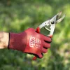 A gloved hand holding pruning shears against a blurred green background. Náhled obrázku produktu
