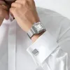 A man's wrist wearing a silver watch and cufflinks, with a white shirt. Produktbild-Vorschau