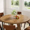 A round wooden dining table with a vase of flowers and a bowl of fruit, set in a bright room with large windows overlooking a green landscape. Anteprima dell’immagine prodotto