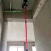 A laser level mounted on a telescopic pole is being used to project a green laser line on a ceiling in a room under construction. Produktbild-Vorschau