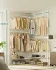 A corner clothing rack system with various garments hanging on it. Several storage boxes and shoes are placed on the shelves and floor below. A suitcase is partially visible on the right. Produktbild-Vorschau