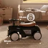 A black retro ride-on car for children is shown in a bedroom setting, next to a bed and a wooden dresser. Náhled obrázku produktu