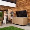 A couple is placing cushions into a large outdoor storage box on a patio. Produktbild-Vorschau