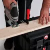 A person is using a jigsaw to cut a piece of wood, which is clamped to a black toolbox. Náhled obrázku produktu
