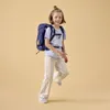 A young girl wearing a backpack and striped pants poses against a plain background. Podgląd zdjęcia produktu